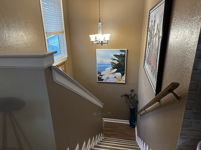 staircase with wood finished floors and an inviting chandelier