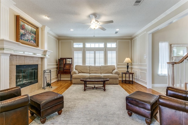 living area with crown molding, visible vents, a decorative wall, wood finished floors, and a tile fireplace