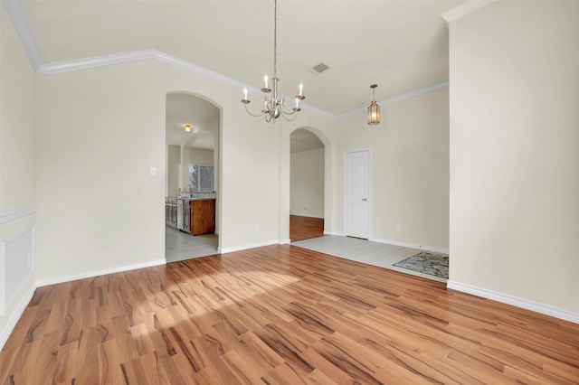 spare room featuring visible vents, baseboards, light wood-style flooring, ornamental molding, and an inviting chandelier