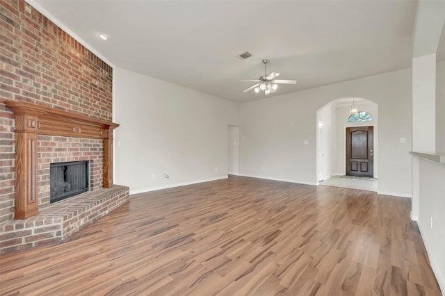 unfurnished living room featuring ceiling fan, arched walkways, a fireplace, and wood finished floors