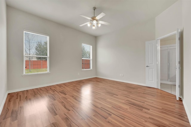 spare room featuring lofted ceiling, baseboards, ceiling fan, and light wood finished floors