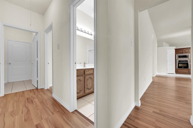 hall with light wood-type flooring, a sink, and baseboards