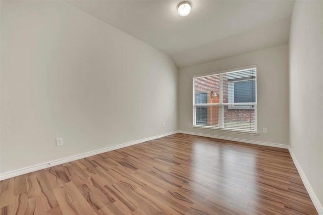 empty room with vaulted ceiling, wood finished floors, and baseboards