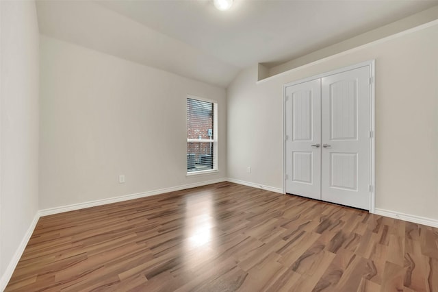 unfurnished bedroom featuring baseboards, vaulted ceiling, and wood finished floors