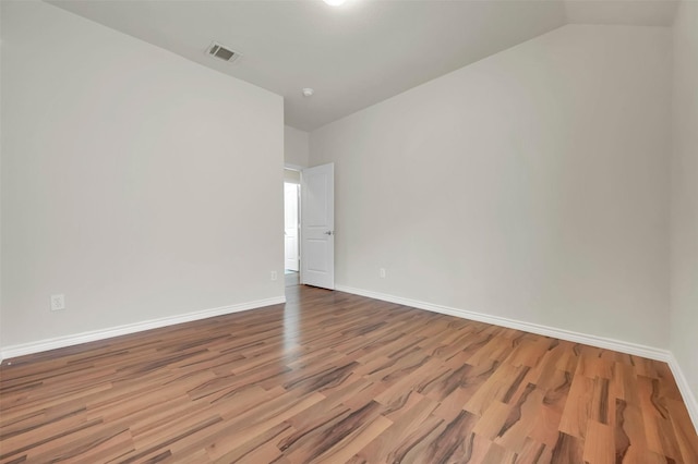 spare room with vaulted ceiling, wood finished floors, visible vents, and baseboards