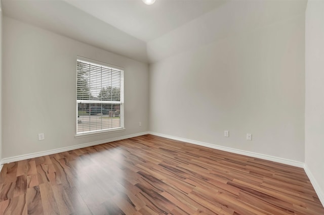 empty room featuring lofted ceiling, wood finished floors, and baseboards