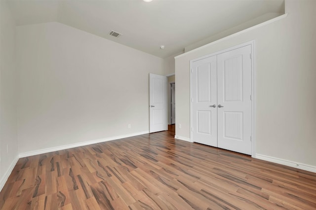 unfurnished bedroom with a closet, visible vents, baseboards, and wood finished floors