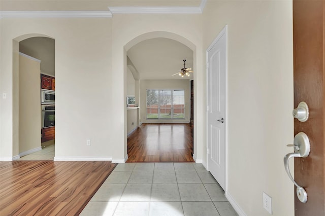 hall featuring baseboards, light tile patterned flooring, arched walkways, and crown molding