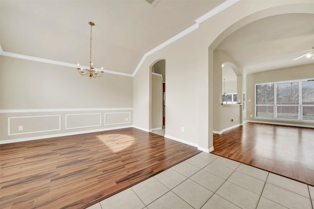 unfurnished room featuring arched walkways, lofted ceiling, light tile patterned flooring, ceiling fan with notable chandelier, and crown molding