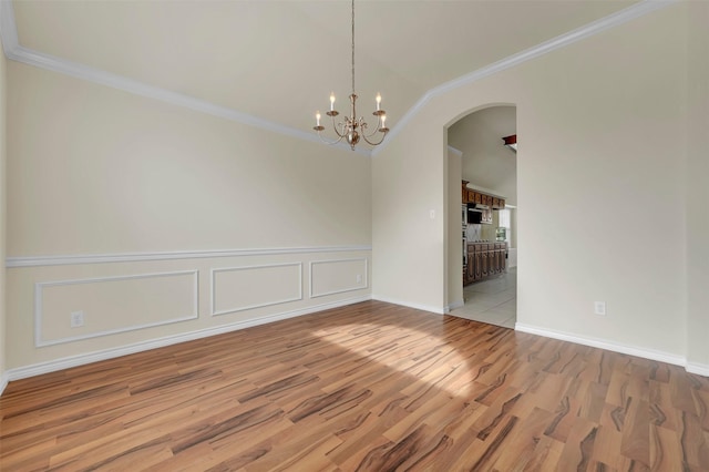 empty room featuring arched walkways, ornamental molding, wood finished floors, and an inviting chandelier