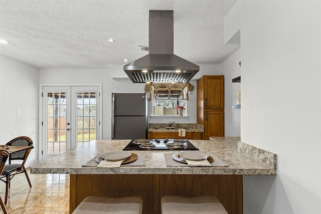 kitchen with cooktop, french doors, island exhaust hood, freestanding refrigerator, and a peninsula