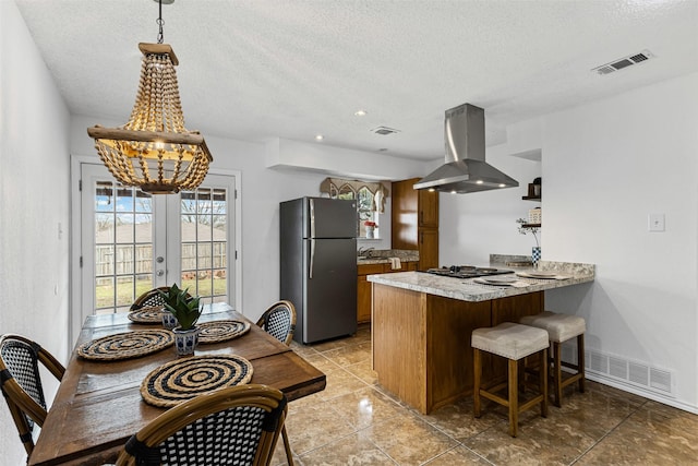 kitchen with island exhaust hood, a sink, freestanding refrigerator, a peninsula, and brown cabinetry