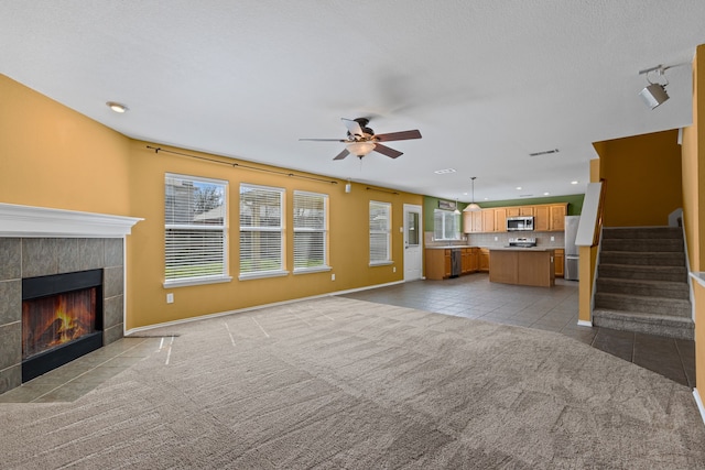 unfurnished living room with light tile patterned floors, visible vents, stairway, a tiled fireplace, and light carpet