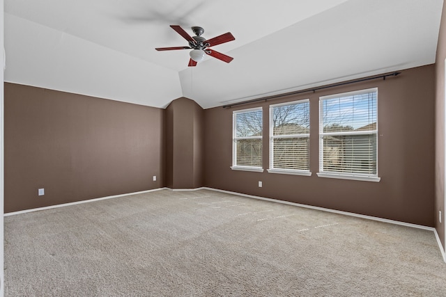 empty room featuring vaulted ceiling, carpet floors, a ceiling fan, and baseboards