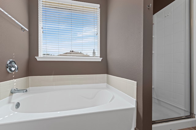 bathroom featuring a shower stall, a bath, and a textured wall