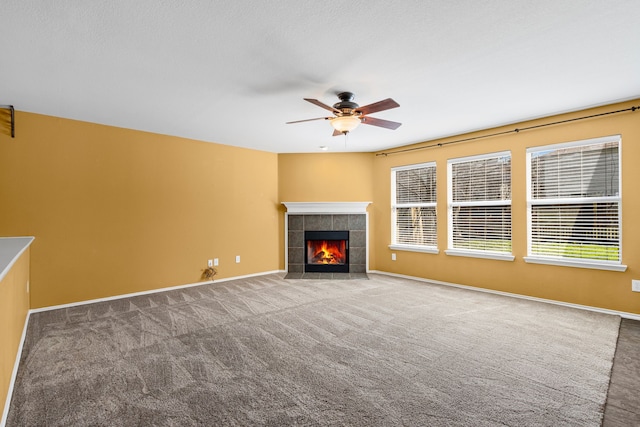 unfurnished living room with ceiling fan, a tiled fireplace, carpet flooring, and baseboards