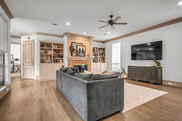 living room with visible vents, wood finished floors, crown molding, a brick fireplace, and recessed lighting