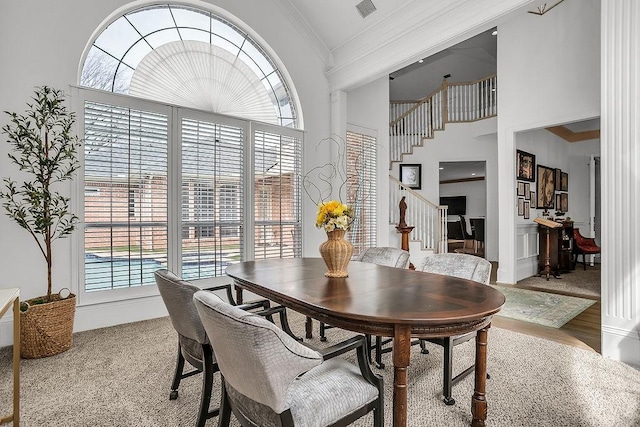 dining space featuring visible vents, a towering ceiling, stairs, crown molding, and light wood-type flooring