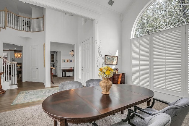 dining room with visible vents, stairway, a high ceiling, ornamental molding, and wood finished floors