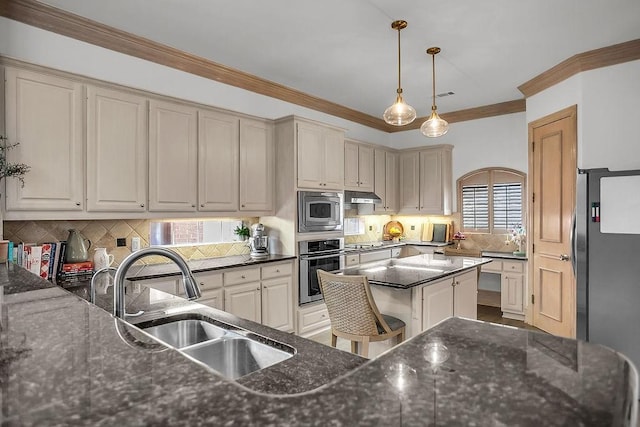 kitchen with appliances with stainless steel finishes, cream cabinets, crown molding, under cabinet range hood, and a sink