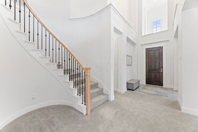 carpeted foyer with stairs, a high ceiling, and baseboards