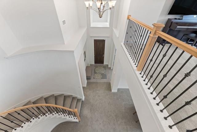 carpeted foyer entrance with stairway, a high ceiling, visible vents, and a chandelier