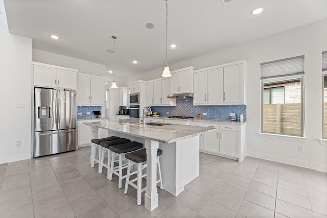 kitchen with light tile patterned floors, a sink, white cabinetry, appliances with stainless steel finishes, and a center island with sink