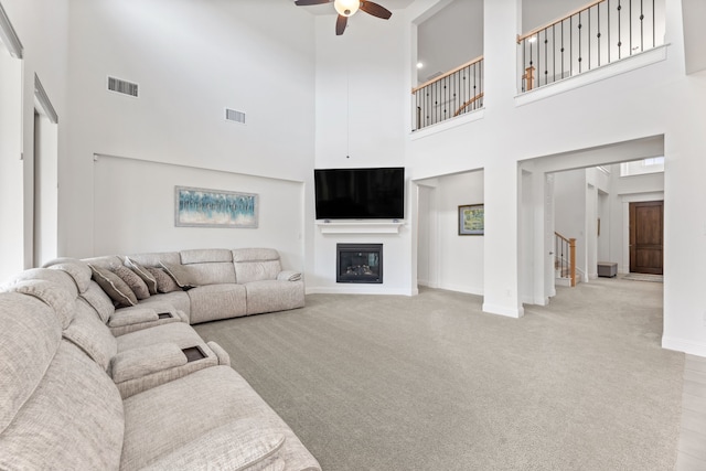 living room with stairs, ceiling fan, a glass covered fireplace, and visible vents