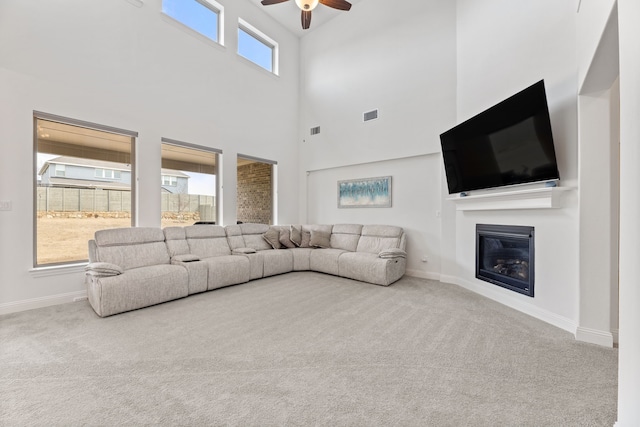 living area with ceiling fan, carpet floors, a glass covered fireplace, and baseboards