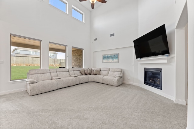 carpeted living room with a ceiling fan, baseboards, a glass covered fireplace, and visible vents