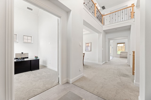 hallway with a towering ceiling, carpet, tile patterned floors, and visible vents