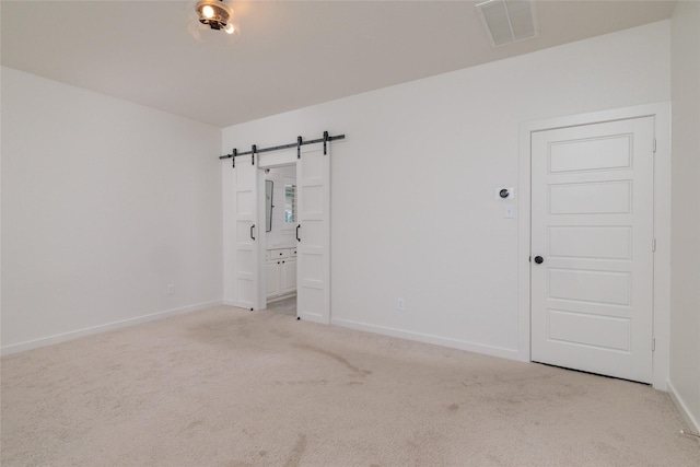 carpeted spare room with a barn door, visible vents, and baseboards