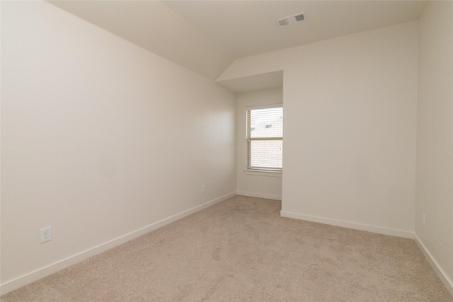 empty room with baseboards, visible vents, vaulted ceiling, and light colored carpet