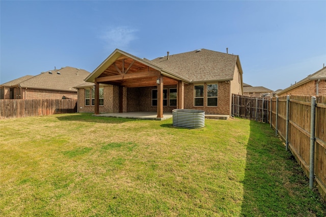 back of house with brick siding, a fenced backyard, a lawn, and a patio