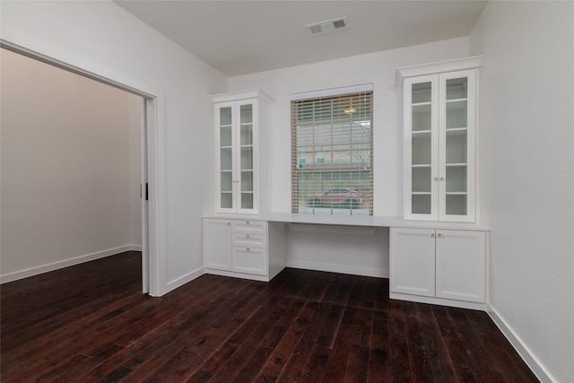 unfurnished office with baseboards, visible vents, dark wood-style flooring, and built in desk