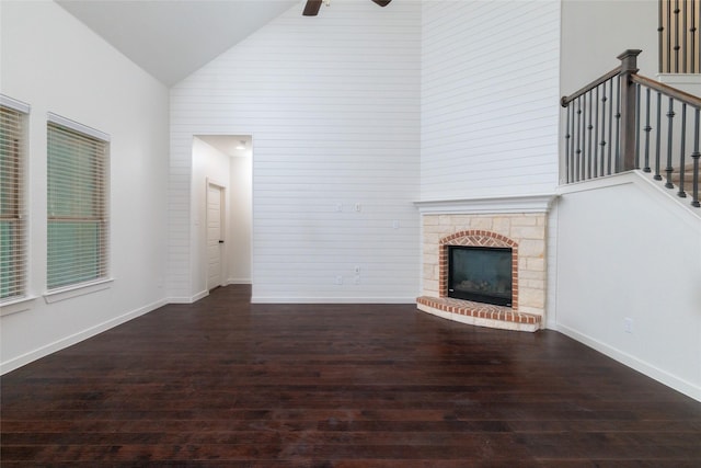 unfurnished living room with baseboards, high vaulted ceiling, a fireplace with raised hearth, and wood finished floors