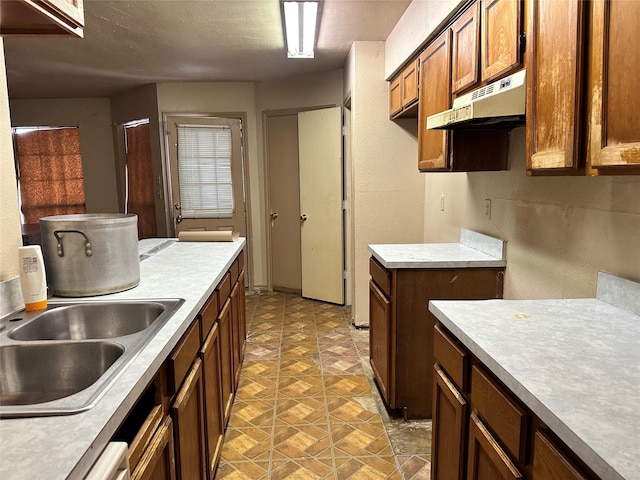 kitchen featuring brown cabinetry, light countertops, a sink, and under cabinet range hood