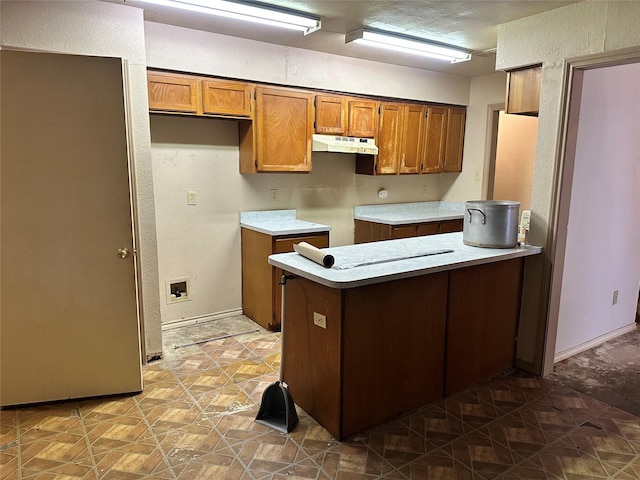 kitchen with white electric stovetop, brown cabinets, a peninsula, light countertops, and under cabinet range hood