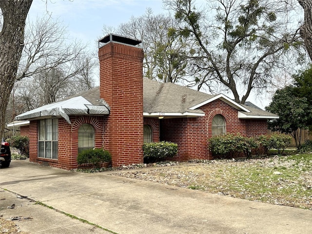 ranch-style house with brick siding, a chimney, and a shingled roof