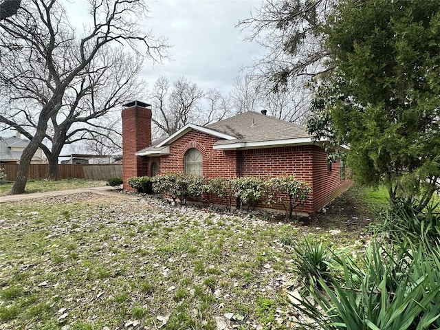 view of front of property with brick siding, roof with shingles, a chimney, and fence