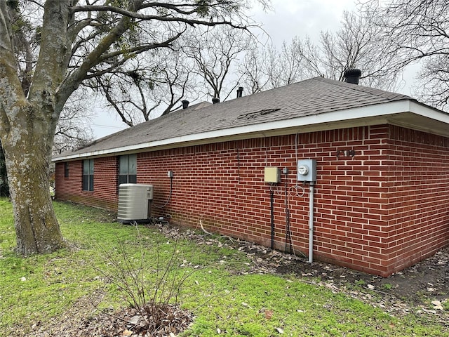 view of home's exterior with central air condition unit, a yard, a shingled roof, and brick siding