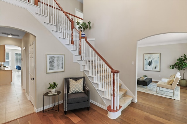 stairs with visible vents, wood finished floors, arched walkways, baseboards, and a towering ceiling