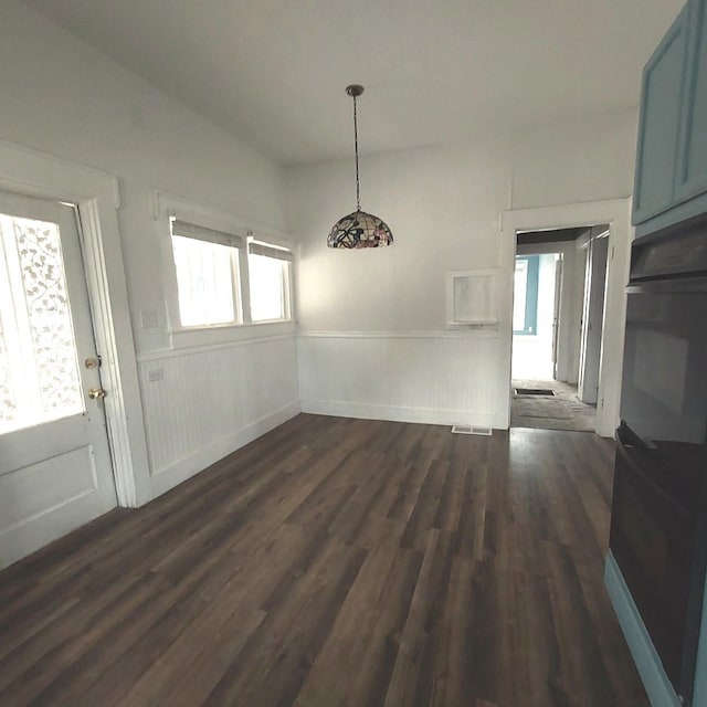 unfurnished dining area featuring wainscoting and dark wood finished floors