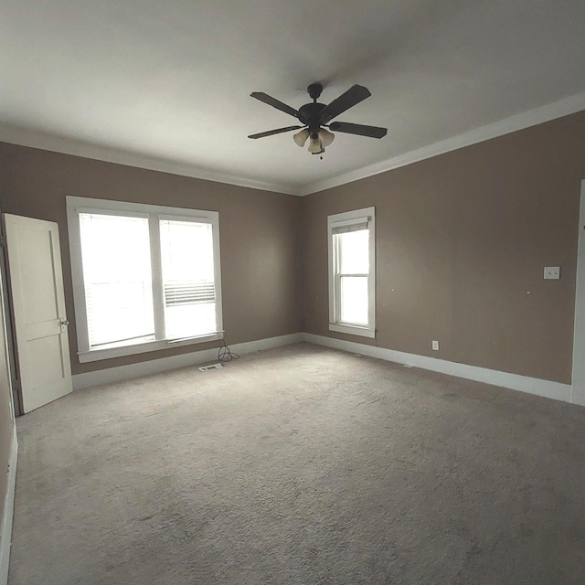 carpeted spare room featuring visible vents, ornamental molding, a ceiling fan, and baseboards