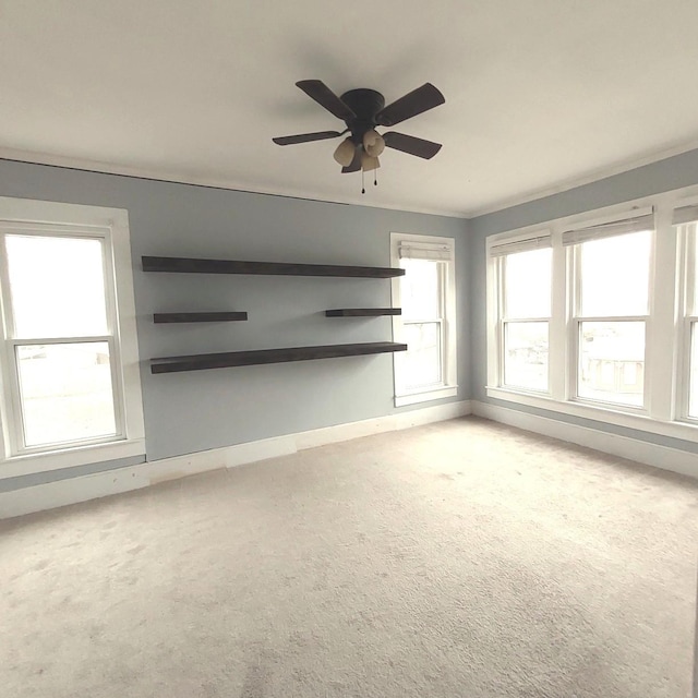 unfurnished living room featuring carpet floors, ornamental molding, baseboards, and a ceiling fan