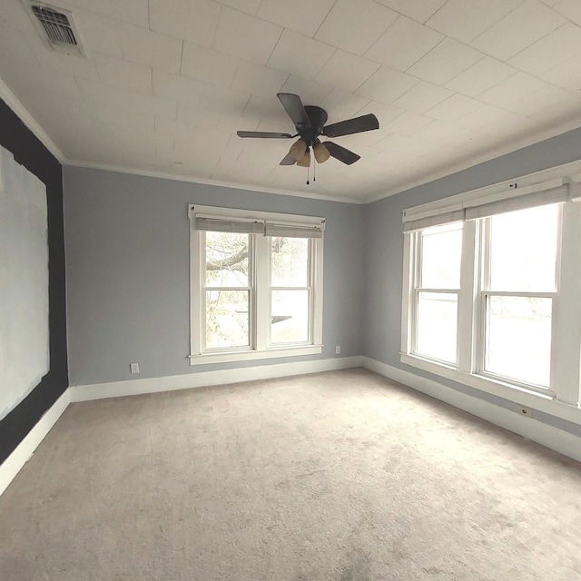 carpeted empty room featuring baseboards, ceiling fan, visible vents, and crown molding