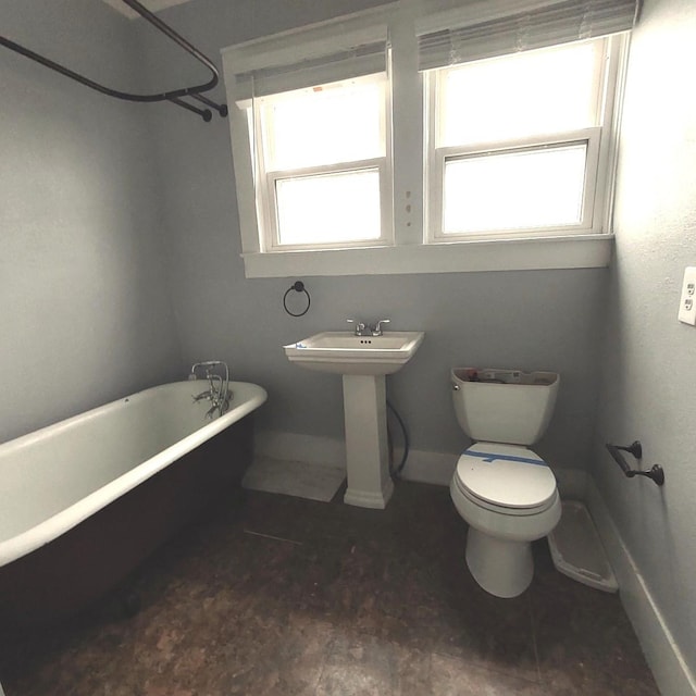 full bathroom featuring toilet, a soaking tub, baseboards, and a sink