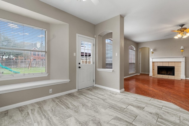 foyer entrance with ceiling fan, a fireplace, arched walkways, and baseboards