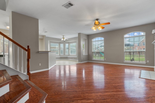 unfurnished living room with stairs, a wealth of natural light, wood finished floors, and visible vents