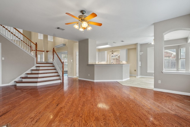 unfurnished living room with light wood finished floors, visible vents, ceiling fan, baseboards, and stairs